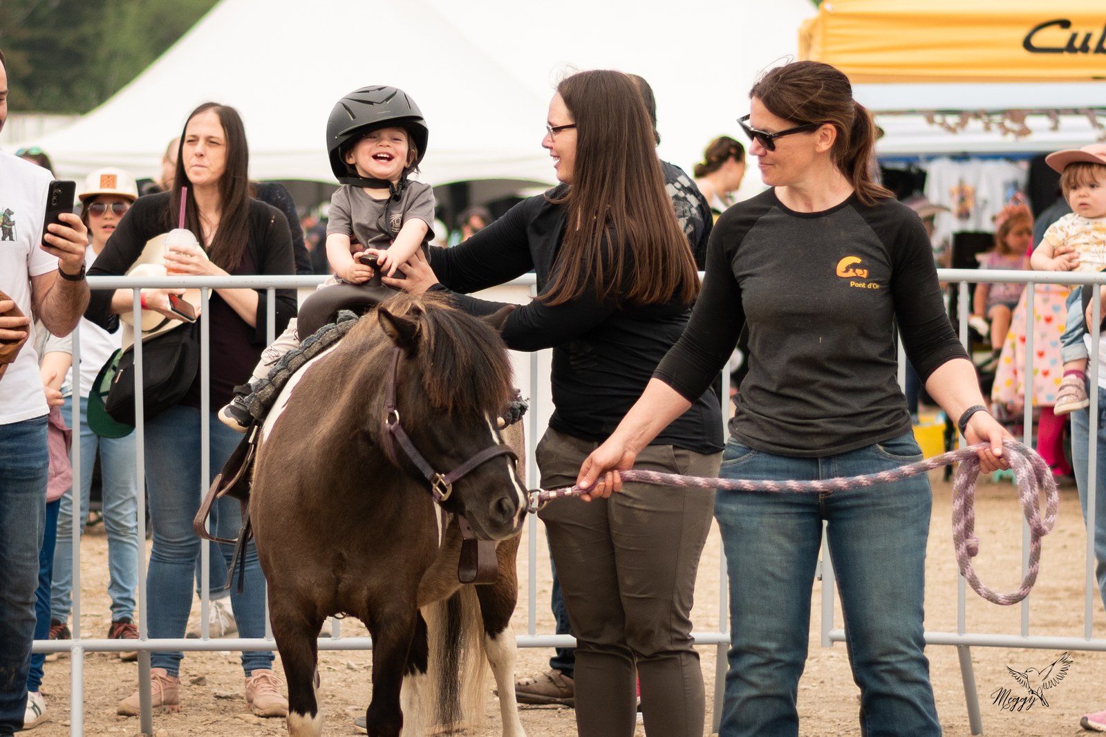 Un enfant souriant sur un poney, accompagné par des adultes au Festival.